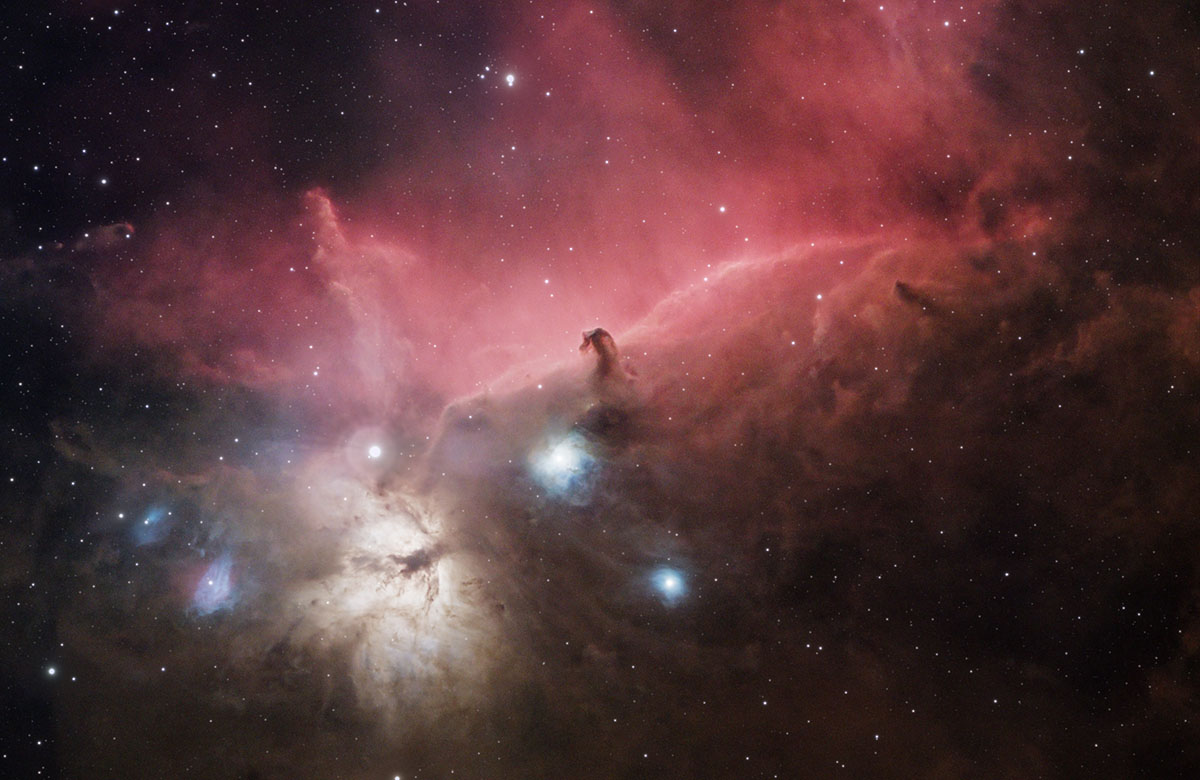 Central to the image is the Horsehead Nebula, a dark, horse-shaped silhouette set against a backdrop of red hydrogen clouds, glowing with the light of nearby stars. To the lower right corner is the Flame Nebula, a fiery, glowing region of interstellar dus